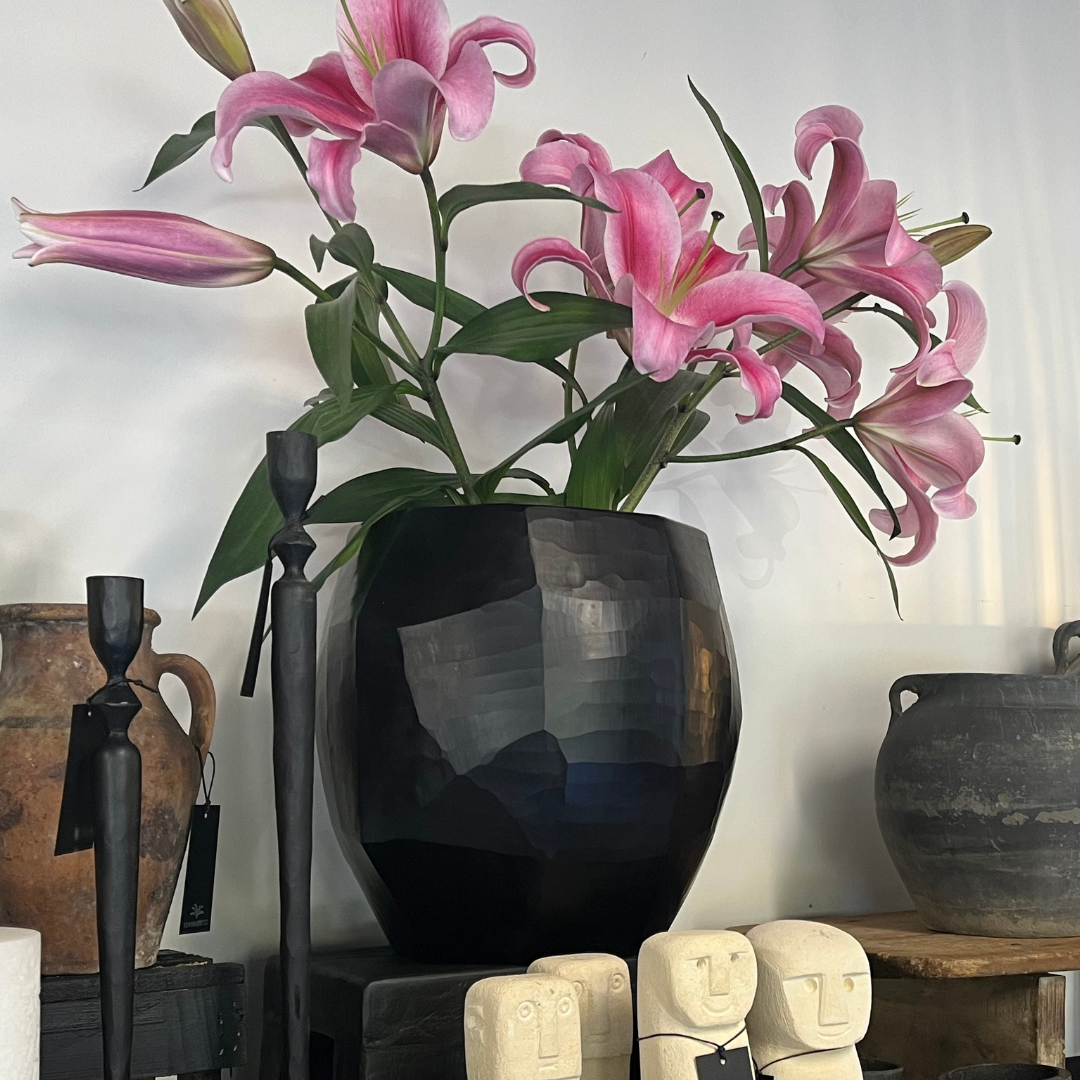 Indigo Love Sculpt Black Vase - Large - high-quality opaque black glass with polygon shapes and geometric design - art that doubles as a functional vase or candle/tealight lantern - Shown on shop display with Lilly flowers around other home decor - Stocked at LOVINLIFE Co Byron Bay for all your gifts, candles and interior decorating needs