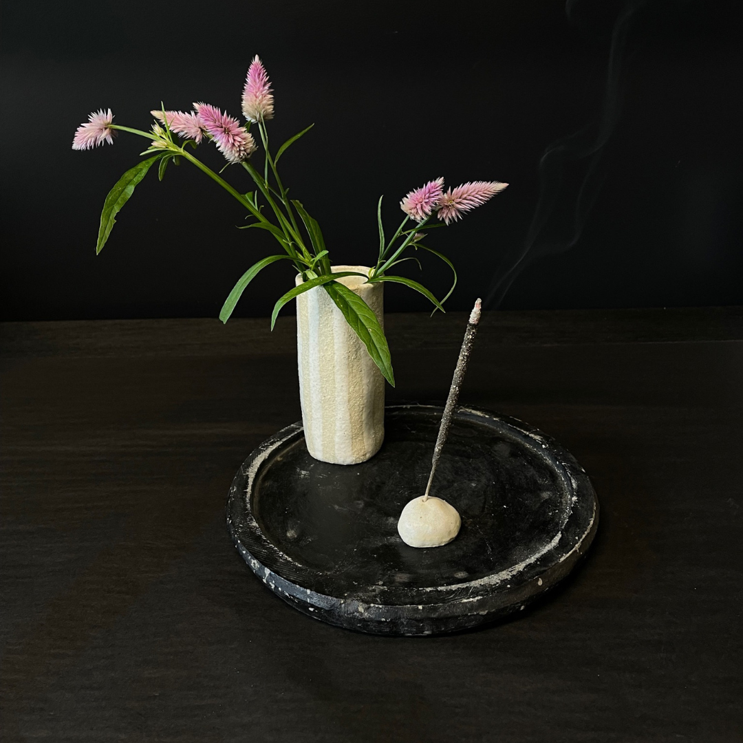 Lovinlife Co ByronBay – handmade Ceramic Pebble Incense Holder to hold your favourite incense – pictured holding smoking incense stick next to stripe handmade ceramic vase with flowers - available at LOVINLIFE Co Byron Bay for all your gifts, candles and interior decorating needs