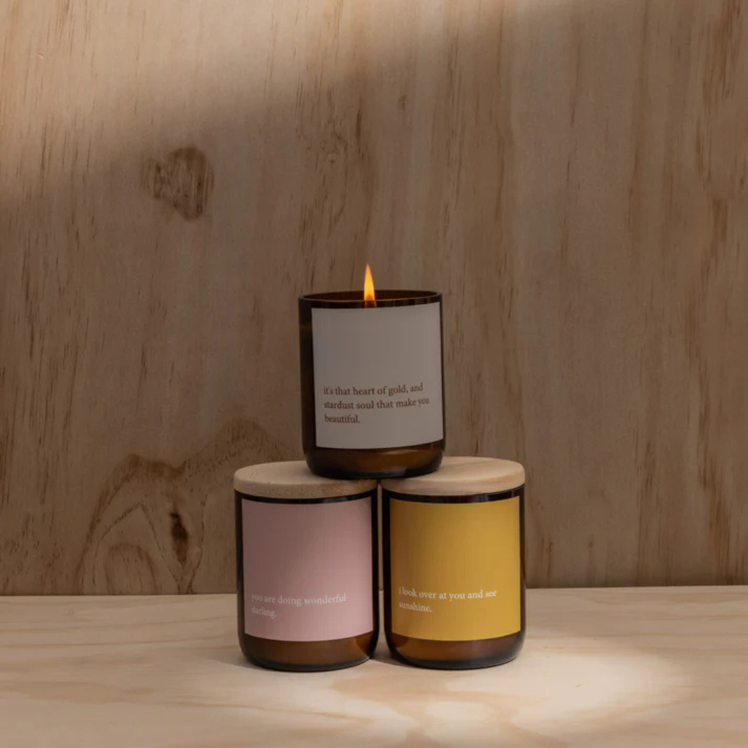 Commonfolk Heartfelt Candle - Wanaka scent with geranium + lavender - "I look over at you and see Sunshine" jar pictured on plywood backdrop, with with two other heartfelt candles stacked - Stocked at LOVINLIFE Co Byron Bay for all your gifts, candles and interior decorating needs