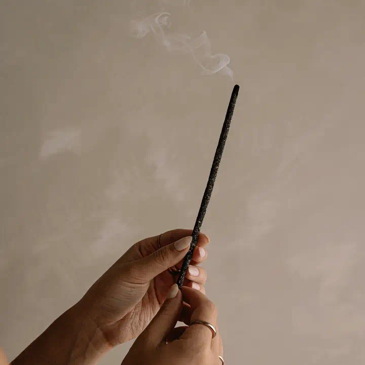 Cedar and Myrrh Black Copal Hand Rolled Incense Stick - smoking being held by two hands - Stocked at LOVINLIFE Co Byron Bay for all your gifts, candles and interior decorating needs