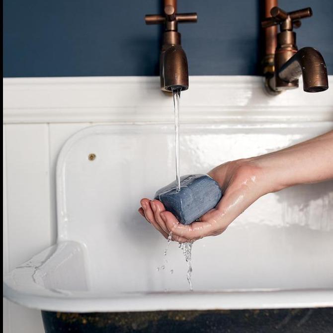 Lovinlife Co ByronBay – Saarde Charcoal Olive Oil Bar Soap – Activated Charcoal for deep cleaning, gentle exfoliation, absorbing excess oil - unscented – soap bar pictured being held under running water in vintage metal sink - available at LOVINLIFE Co Byron Bay for all your gifts, candles and interior decorating needs