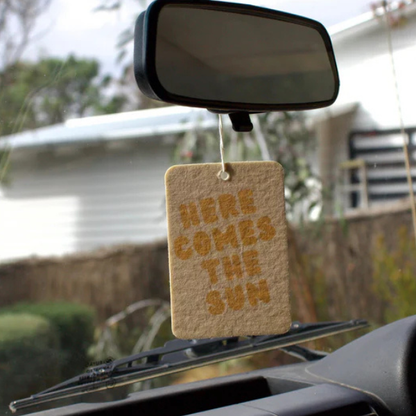 Here Comes The Sun design Air Freshener tags - Made from 100% post-consumer materials - BIARRITZ SCENT: jasmine, saffron + musk, Feel allured as you indulge in this poetic union that is luxe and luminous, yet grounding - Pictured hanging from rear vision mirror. Stocked at LOVINLIFE Co Byron Bay for all your gifts, candles and interior decorating needs
