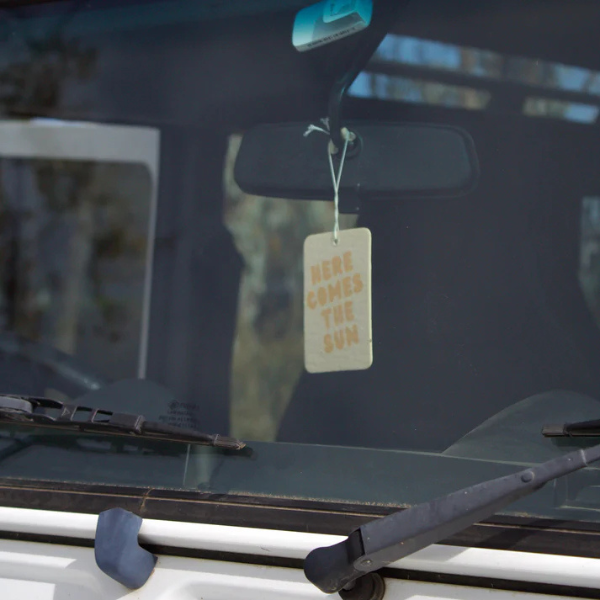 Here Comes The Sun design Air Freshener tags - Made from 100% post-consumer materials - BIARRITZ SCENT: jasmine, saffron + musk, Feel allured as you indulge in this poetic union that is luxe and luminous, yet grounding - Pictured hanging from rear vision mirror. Stocked at LOVINLIFE Co Byron Bay for all your gifts, candles and interior decorating needs