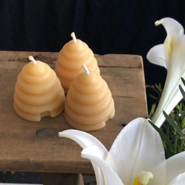 Three pure beeswax candles shaped like beehives on a wooden surface with white flowers in the foreground. Stocked at LOVINLIFE Co Byron Bay for all your gifts, candles and interior decorating needs