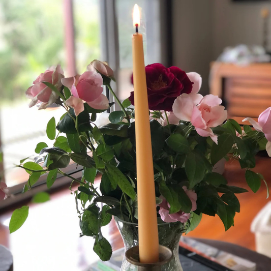 Vase with pink and red roses and a tall yellow pure beeswax taper candle on a blurred indoor background. Stocked at LOVINLIFE Co Byron Bay for all your gifts, candles and interior decorating needs