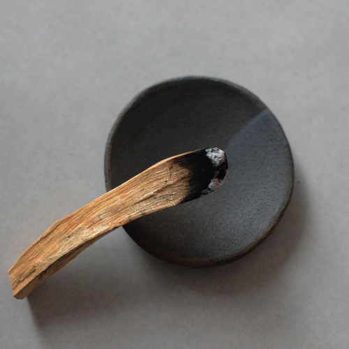 Black Clay Incense Plate - Handcrafted smudging bowl or plate pictured from above with smoking palo santo stick resting on it - Stocked at LOVINLIFE Co Byron Bay for all your gifts, candles and interior decorating needs