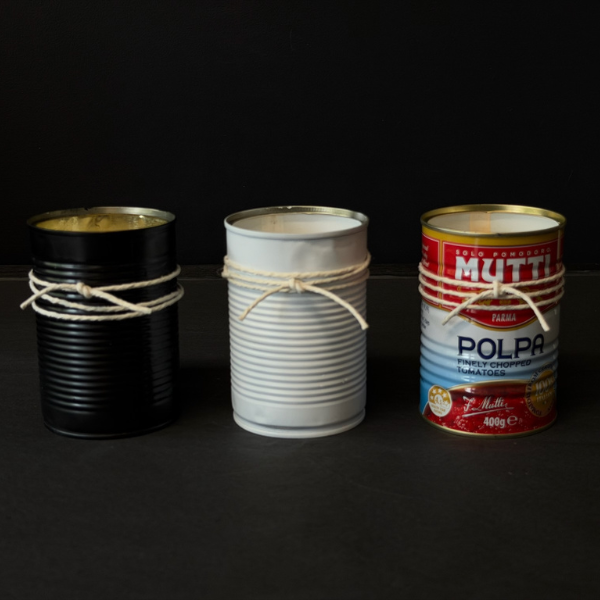 Three recycled Mutti Polpa tins that've been turned into candles on a dark surface. Designed for outdoors (although can be indoors too) these Hand made candles are fragranced with Citronella and Lemongrass with a touch of Lavender. Recycled tins are filled with soy/plant based wax blended with pure essential oils, intended as a mild deterrent for annoying bugs. Available at LOVINLIFE Co Byron Bay.