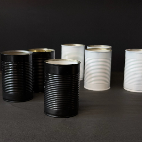 Collection of recycled Black & White tins that've been turned into candles on a dark surface. Designed for outdoors (although can be indoors too) these Hand made candles are fragranced with Citronella and Lemongrass with a touch of Lavender. Recycled tins are filled with soy/plant based wax blended with pure essential oils, intended as a mild deterrent for annoying bugs. Available at LOVINLIFE Co Byron Bay.
