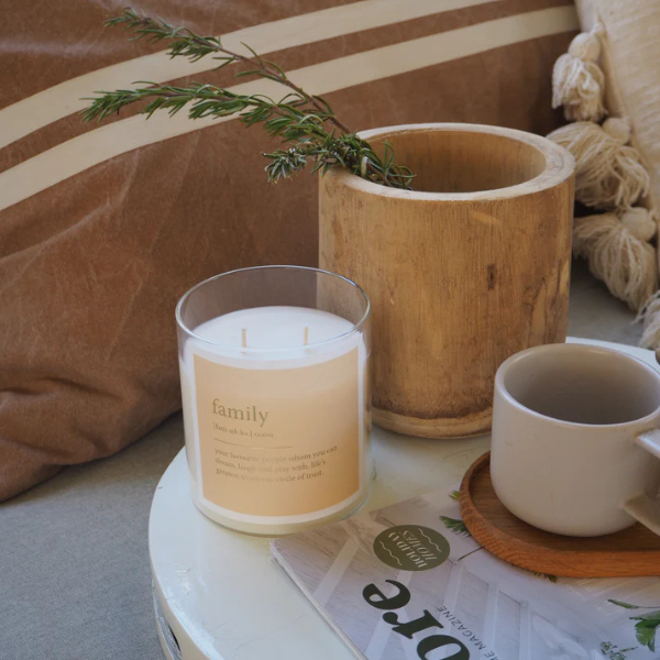 Candle labelled 'family' on a table with a mug, plant, and newspaper. These Goldie Dictionary Candles are a little bit luxe, and will surely make your favourite folks feel super special. Featuring luxe gold foil on a matte textured label, these are a stand out. Available at LOVINLIFE Co Byron Bay