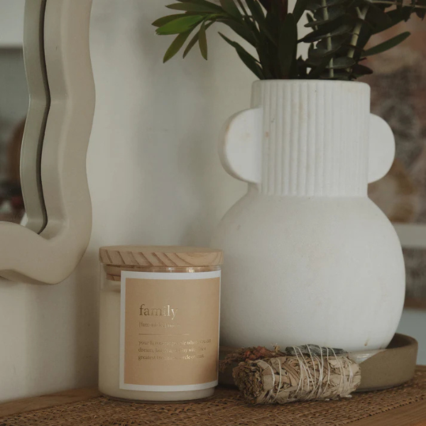 White vase, candle labelled 'family', and decorative item on a surface with a blurred background. These Goldie Dictionary Candles are a little bit luxe, and will surely make your favourite folks feel super special. Featuring luxe gold foil on a matte textured label, these are a stand out. Available at LOVINLIFE Co Byron Bay