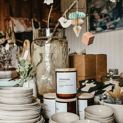 Decorative items including plates, jars, and a candle labelled 'Christmas' in a home setting. These Dictionary Meaning Candles are some of our most loved products. We have spent an abundance of time, curating our own meanings of the words to help you feel connected, to help you tell someone how you feel in a unique way. Available at LOVINLIFE Co Byron Bay