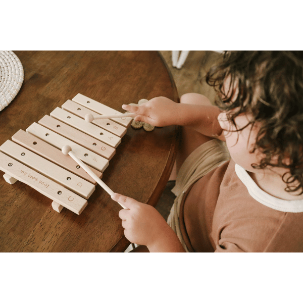 Child playing with Little Noted Xylophone made with FSC certified Birch & Beechwood, and Metal. One of a kind hand-crafted and exclusively in house designed 8 key xylophone (x2 mallets & cotton canvas bag included). Made with Wood, iron and leather. All  instruments by Love Note Co are handmade items, non-toxic, eco-friendly and sustainably sourced. Stocked at LOVINLIFE Co Byron Bay for all your gifts, candles and interior decorating needs