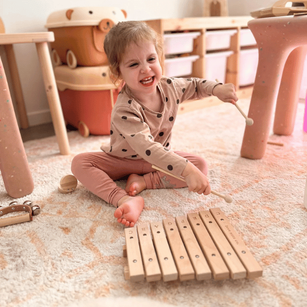 Child playing with Little Noted Xylophone on the carpet. Instrument made with FSC certified Birch & Beechwood, and Metal. One of a kind hand-crafted and exclusively in house designed 8 key xylophone (x2 mallets & cotton canvas bag included). Made with Wood, iron and leather. All  instruments by Love Note Co are handmade items, non-toxic, eco-friendly and sustainably sourced. Stocked at LOVINLIFE Co Byron Bay for all your gifts, candles and interior decorating needs