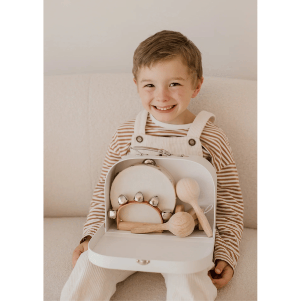 Child with Little Love Music Set resting in his lap. Set includes: Maracas (x2) Castanets (x2) Tambourine Drum (x1) Hand bells (x1)  Suitcase (x1). Comes with a beautiful in house designed suitcase to pack up and store the instruments in. Made with Wood, iron and leather. All  instruments by Love Note Co are handmade items, non-toxic, eco-friendly and sustainably sourced. Stocked at LOVINLIFE Co Byron Bay for all your gifts, candles and interior decorating needs