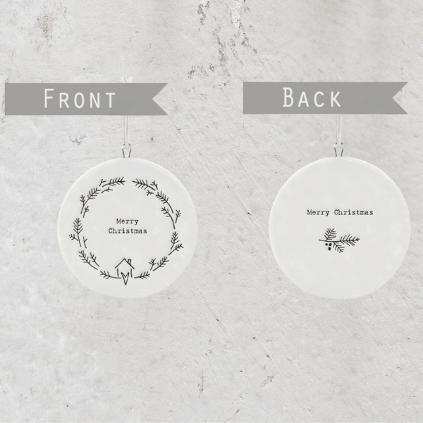 White, round porcelain Christmas decoration finished with simple hand-drawn style illustrations of a  Christmas wreath made of holly, and the phrase “Merry Christmas”. Made by East of India in the UK, available at LOVINLIFE Co Byron Bay