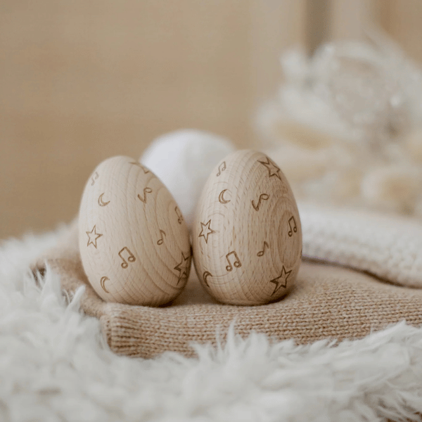 2 x wooden egg shakers by Love Note Co resting on blankets. Made with FSC certified Beechwood. All  instruments by Love Note Co are handmade items, non-toxic, eco-friendly and sustainably sourced. Stocked at LOVINLIFE Co Byron Bay for all your gifts, candles and interior decorating needs