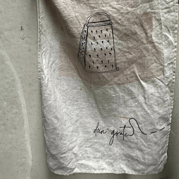 French Linen Tea Towel pictured hanging to show a sketch of a grater and the words "doin grater..." printed underneath. Designed in Australia, Heaven In Earth, available at LOVINLIFE Co Byron Bay