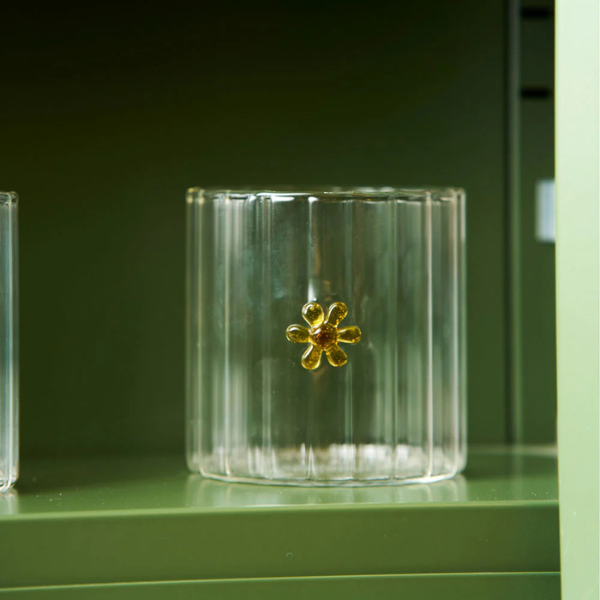 Clear glass tumbler with a yellow flower, pictured on a green shelf. Part of the Robert Gordon Collection stocked at LOVINLIFE Co Byron Bay for all your gifts, candles, homewares and interior decorating needs
