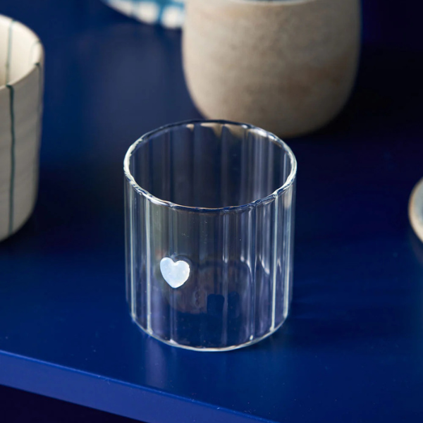 Clear glass tumbler with a white heart design, pictured on a blue surface. Part of the Robert Gordon Collection stocked at LOVINLIFE Co Byron Bay for all your gifts, candles, homewares and interior decorating needs
