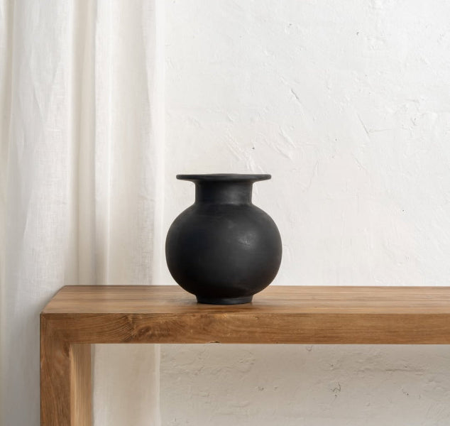 Black vase on a wooden table against a white wall