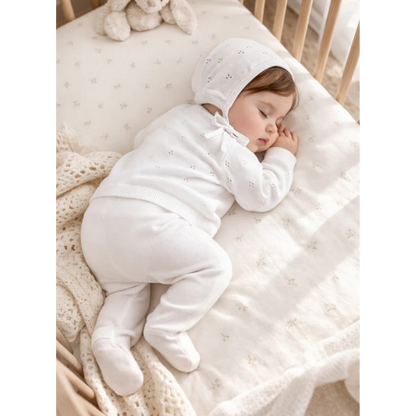 Baby sleeping in a crib showcasing an 100% organic cotton 4-piece Heirloom Knit Baby Gift Set in white with a plush toy in the background. Set by Aster & Oak and Stocked at LOVINLIFE Co Byron Bay for all your gifts, candles and interior decorating needs