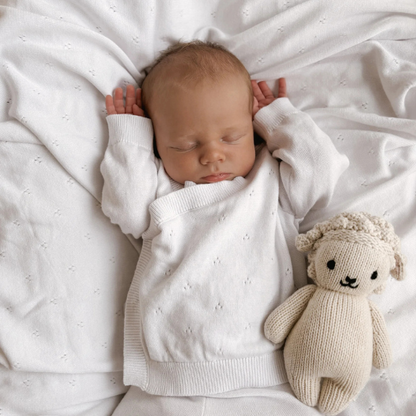 New born Baby sleeping in a crib showcasing an 100% organic cotton 4-piece Heirloom Knit Baby Gift Set in white with a knitted toy by their side. Set by Aster & Oak and Stocked at LOVINLIFE Co Byron Bay for all your gifts, candles and interior decorating needs