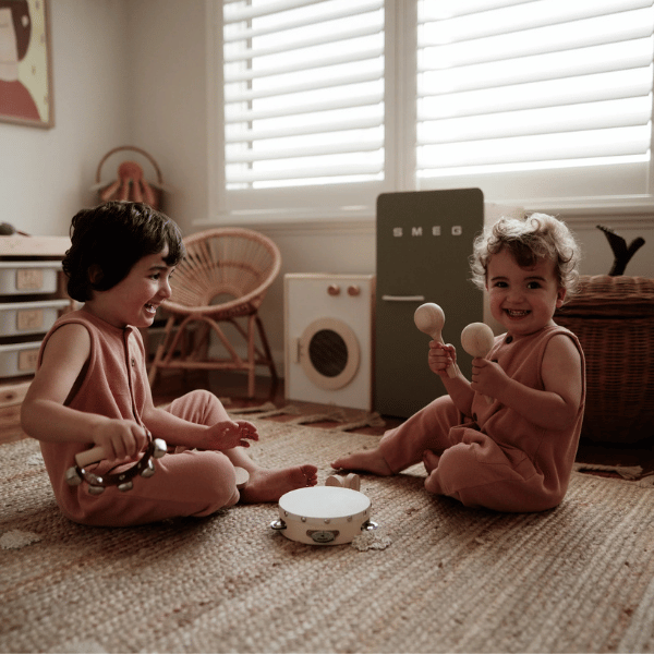 2 x children playing with Little Love Music Set. Set includes: Maracas (x2) Castanets (x2) Tambourine Drum (x1) Hand bells (x1)  Suitcase (x1). Comes with a beautiful in house designed suitcase to pack up and store the instruments in. Made with Wood, iron and leather. All  instruments by Love Note Co are handmade items, non-toxic, eco-friendly and sustainably sourced. Stocked at LOVINLIFE Co Byron Bay for all your gifts, candles and interior decorating needs