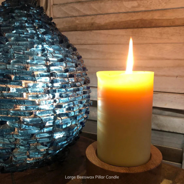 Large pure Beeswax pillar candle on a wooden surface next to a decorative blue glass lamp. Stocked at LOVINLIFE Co Byron Bay for all your gifts, candles and interior decorating needs