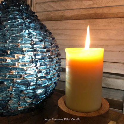 Large pure Beeswax pillar candle on a wooden surface next to a decorative blue glass lamp. Stocked at LOVINLIFE Co Byron Bay for all your gifts, candles and interior decorating needs