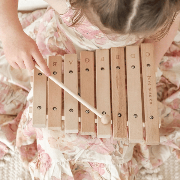 Child playing on Little Noted Xylophone made with FSC certified Birch & Beechwood, and Metal. One of a kind hand-crafted and exclusively in house designed 8 key xylophone (x2 mallets & cotton canvas bag included). Made with Wood, iron and leather. All  instruments by Love Note Co are handmade items, non-toxic, eco-friendly and sustainably sourced. Stocked at LOVINLIFE Co Byron Bay for all your gifts, candles and interior decorating needs