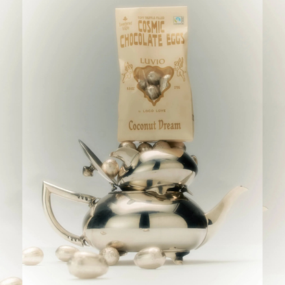 Silver teapot with LOCO LOVE cosmic chocolate eggs in Coconut Dream, and a bag labelled 'Cosmic Chocolate Eggs' on a light gray background. Available at LOVINLIFE Co Byron Bay