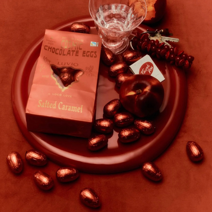 Bag of Loco Love Cosmic Eggs - Salted Caramel Luvia Cosmic Chocolate Eggs on a red plate with a glass of water and a card. Available at LOVINLIFE Co Byron bay