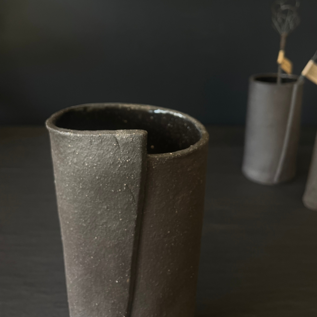 Lovinlife Co ByronBay - Handmade Signature Ceramics Range - Dark Matter Slab Series, matt black stone finish clay pieces - Slab Fold Vase 4 pictured in front with two smaller size vases, one holding twisted wire decorations in background - available at LOVINLIFE Co Byron Bay for all your gifts, candles and interior decorating needs