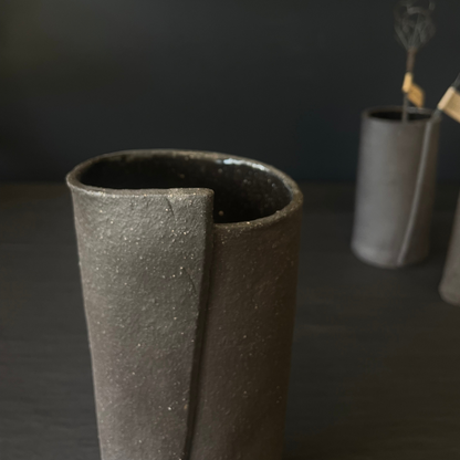 Lovinlife Co ByronBay - Handmade Signature Ceramics Range - Dark Matter Slab Series, matt black stone finish clay pieces - Slab Fold Vase 4 pictured in front with two smaller size vases, one holding twisted wire decorations in background - available at LOVINLIFE Co Byron Bay for all your gifts, candles and interior decorating needs