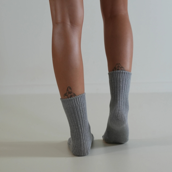 Grey socks on a person’s feet, back view, on a plain background. Luxe Cotton Socks by Number Thirty One made with a soft cotton, wool, and spandex blend. Unisex & One size. Stocked at LOVINLIFE Co Byron Bay for all your gifts, candles and interior decorating needs