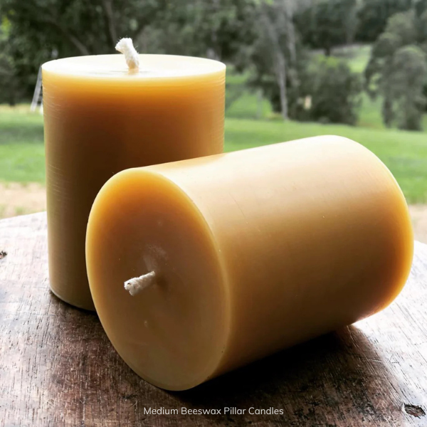 Two medium pure beeswax pillar candles on a wooden surface with a natural background. Stocked at LOVINLIFE Co Byron Bay for all your gifts, candles and interior decorating needs