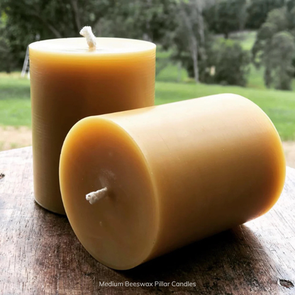 Two medium pure beeswax pillar candles on a wooden surface with a natural background. Stocked at LOVINLIFE Co Byron Bay for all your gifts, candles and interior decorating needs