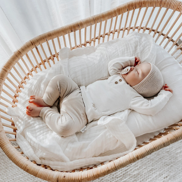 Baby sleeping in a wicker crib on top of an organic muslin cotton baby blanket in white. Stocked at LOVINLIFE Co Byron Bay for all your gifts, candles and interior decorating needs