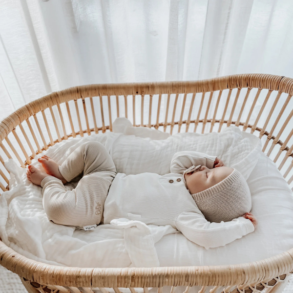 Baby sleeping in a wicker crib on top of an organic muslin cotton baby blanket in white. Stocked at LOVINLIFE Co Byron Bay for all your gifts, candles and interior decorating needs