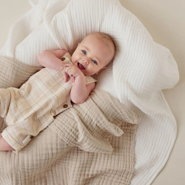 Baby lying on an organic muslin cotton baby blanket in white wearing a beige outfit with buttons. Stocked at LOVINLIFE Co Byron Bay for all your gifts, candles and interior decorating needs