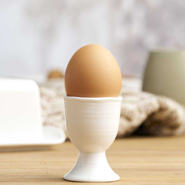 Brown egg in a white ceramic egg cup on a wooden surface with a blurred background. Part of the Robert Gordon Collection stocked at LOVINLIFE Co Byron Bay for all your gifts, candles, homewares and interior decorating needs