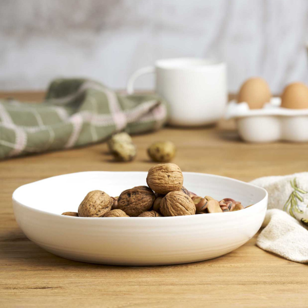 White bowl filled with walnuts on a wooden table with eggs and a mug in the background. Part of the Robert Gordon Collection stocked at LOVINLIFE Co Byron Bay for all your gifts, candles, homewares and interior decorating needs