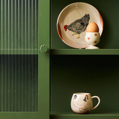 Ceramic plate with a chicken design and an egg on a green shelf, next to a matching ceramic mug. A Henny Penny Chickens design, part of the Robert Gordon Collection stocked at LOVINLIFE Co Byron Bay for all your gifts, candles, homewares and interior decorating needs