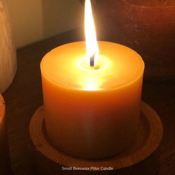 Small beeswax pillar candle with a flame on a dark surface. Stocked at LOVINLIFE Co Byron Bay for all your gifts, candles and interior decorating needs