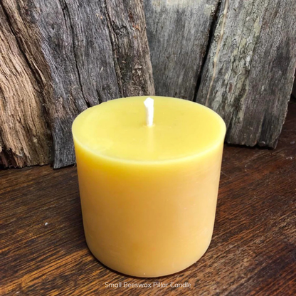 Small pure beeswax pillar candle with pure cotton wick on a wooden surface with a rustic background. Stocked at LOVINLIFE Co Byron Bay for all your gifts, candles and interior decorating needs