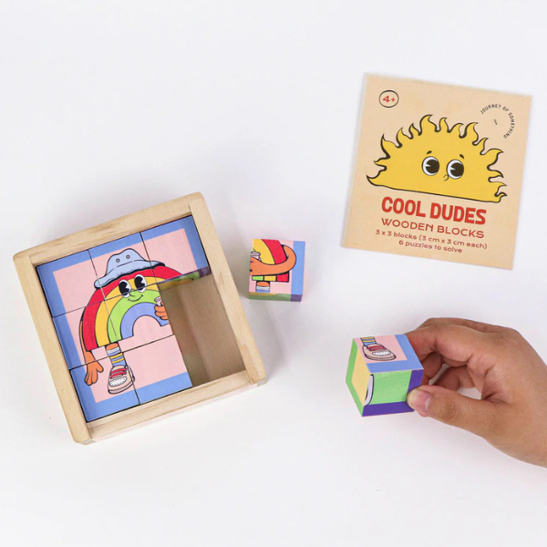 Wooden blocks with colourful designs and a hand interacting with them on a white background. From Wooden Block Puzzle - Cool Dudes - Stocked at LOVINLIFE Co Byron Bay for all your gifts, candles, homewares and interior decorating needs