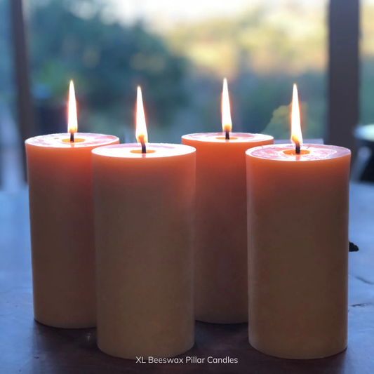 Four lit pure beeswax pillar candles, with a pure cotton wicks, on a wooden surface with a blurred natural background. Stocked at LOVINLIFE Co Byron Bay for all your gifts, candles and interior decorating needs