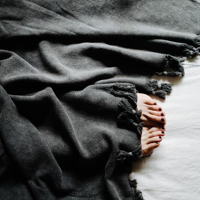 Saarde's Vintage Wash 100% OEKO-TEX® Turkish Cotton Throw Blanket in Charcoal – Pictured from above with toes poking out from underneath - available at LOVINLIFE Co Byron Bay for all your gifts, candles and interior decorating needs