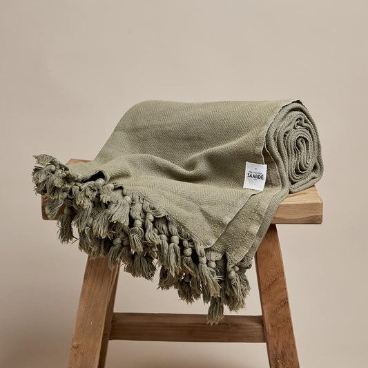 Saarde's Vintage Wash 100% OEKO-TEX® Turkish Cotton Throw Blanket in Olive – Pictured rolled up, resting on small wooden stool - available at LOVINLIFE Co Byron Bay for all your gifts, candles and interior decorating needs