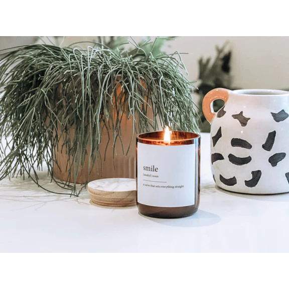 Commonfolk Dictionary Candle - Smile - amber glass jar on table with wood lid on side and plant in pot behind - Stocked at LOVINLIFE Co Byron Bay for all your gifts, candles and interior decorating needs